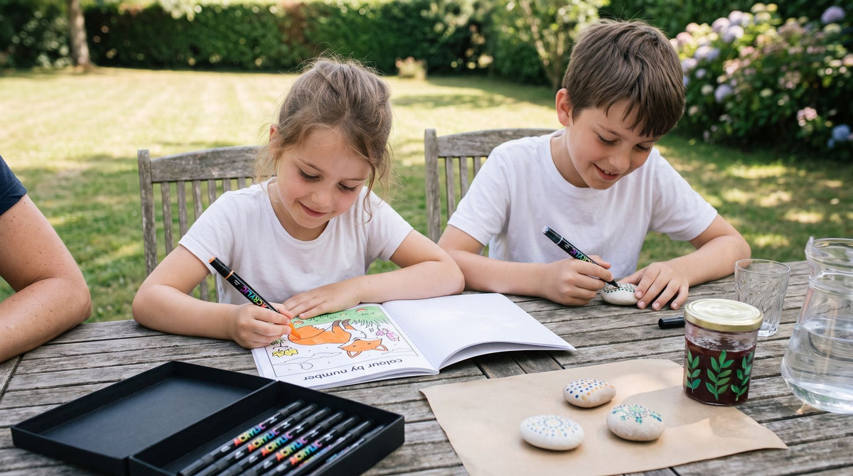 Deux enfants colorient et décorent des galets aux feutres acryliques sur une table de jardin, en été