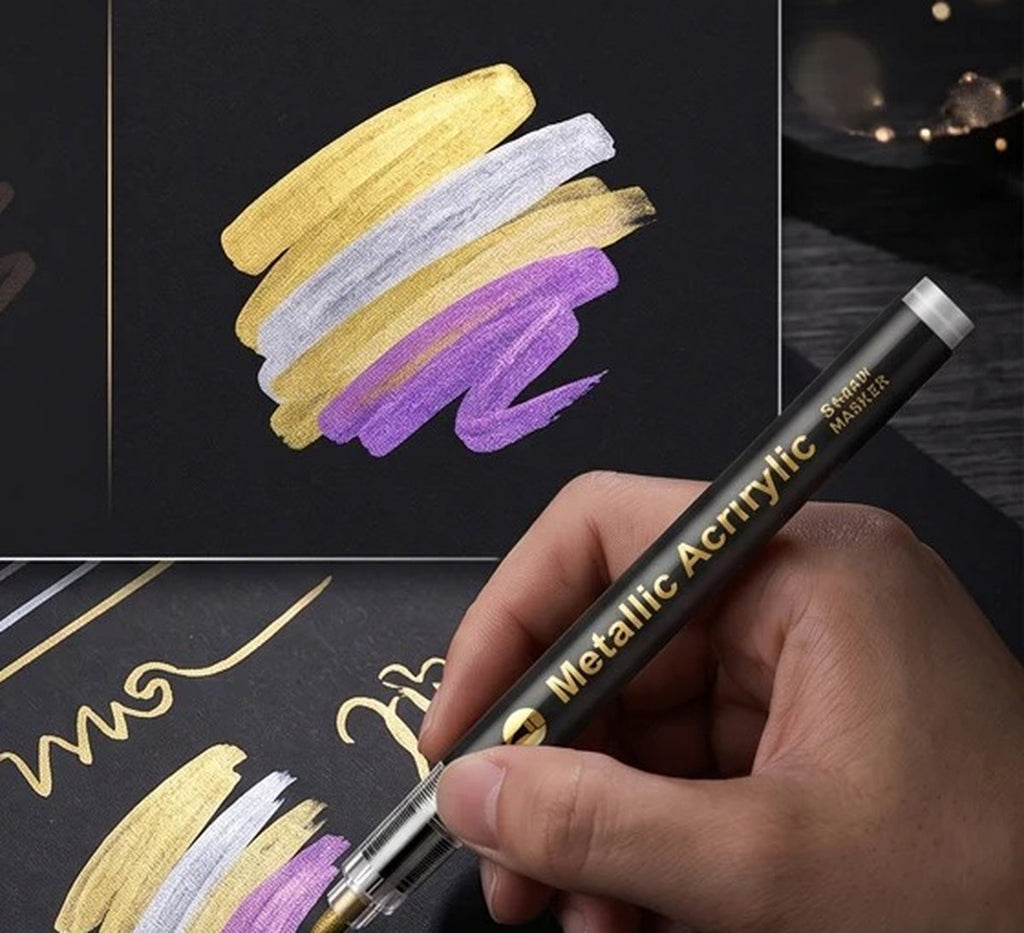 Main qui trace à l'encre métallique or, argent et lilas sur du papier noir